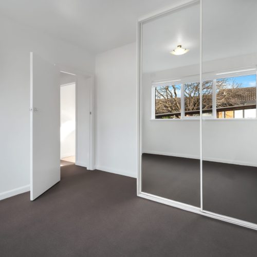 A corner of an empty new room with white walls and a wardrobe with mirror sliding doors